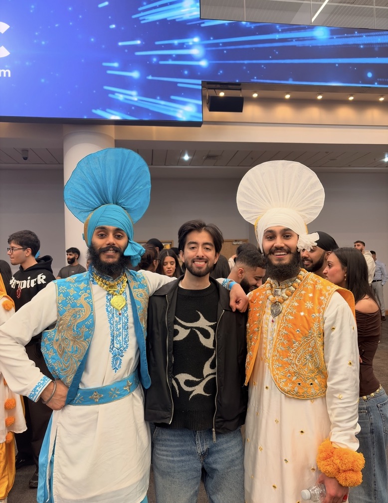 Two LU Bhangra dancers with a guest at an indoor event